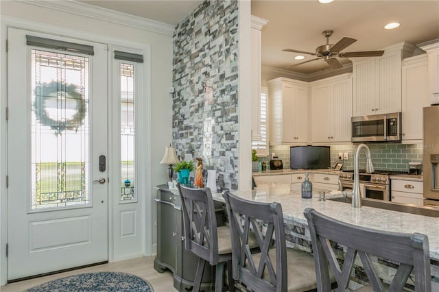 kitchen with a breakfast bar area, stainless steel appliances, light stone countertops, white cabinets, and backsplash