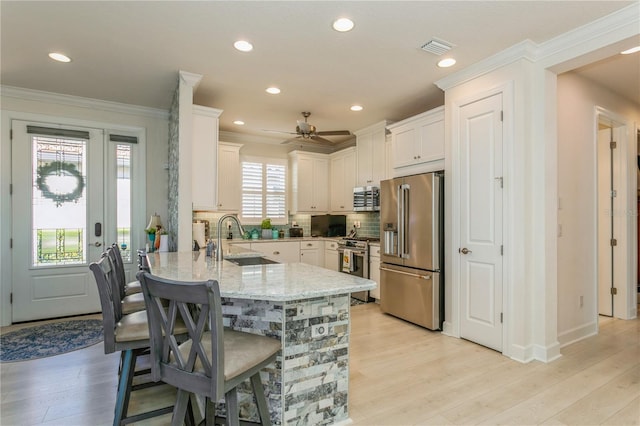 kitchen with light stone counters, kitchen peninsula, stainless steel appliances, white cabinetry, and sink