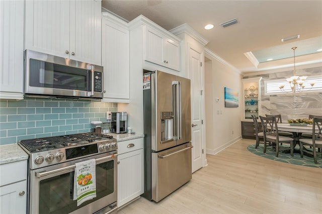 kitchen featuring high end appliances, white cabinets, a tray ceiling, and a notable chandelier