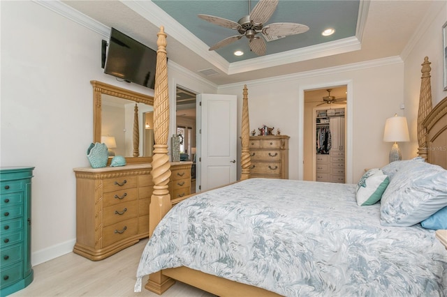 bedroom with a spacious closet, a raised ceiling, a closet, ceiling fan, and ornamental molding