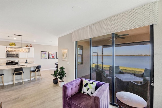 living room featuring a water view, light hardwood / wood-style flooring, ceiling fan, and crown molding