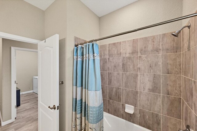 bathroom featuring hardwood / wood-style flooring, shower / bath combo with shower curtain, and washer / clothes dryer