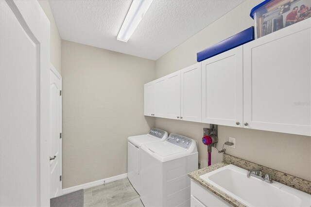 clothes washing area with a textured ceiling, washer and dryer, cabinets, and sink