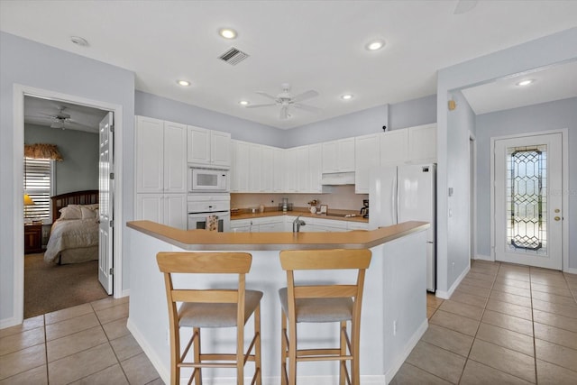 kitchen with white appliances, a kitchen island with sink, white cabinets, light tile patterned flooring, and a breakfast bar area