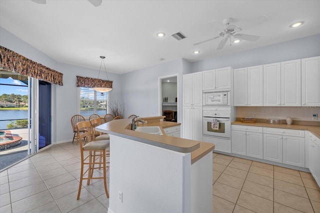 kitchen with white appliances, a center island with sink, sink, decorative light fixtures, and white cabinetry