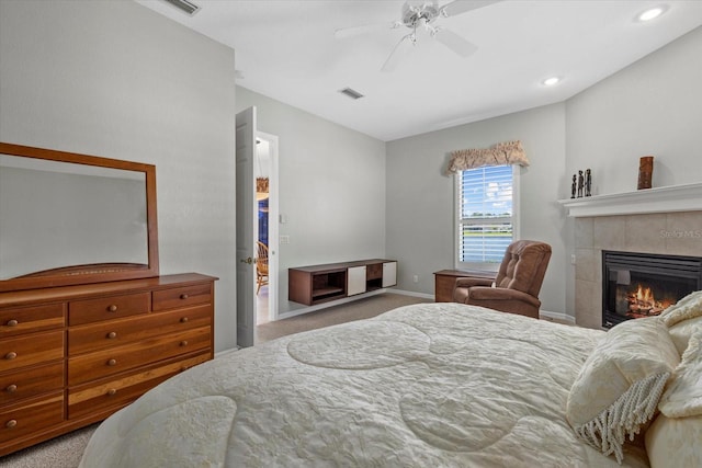 bedroom featuring light carpet, ceiling fan, and a tiled fireplace