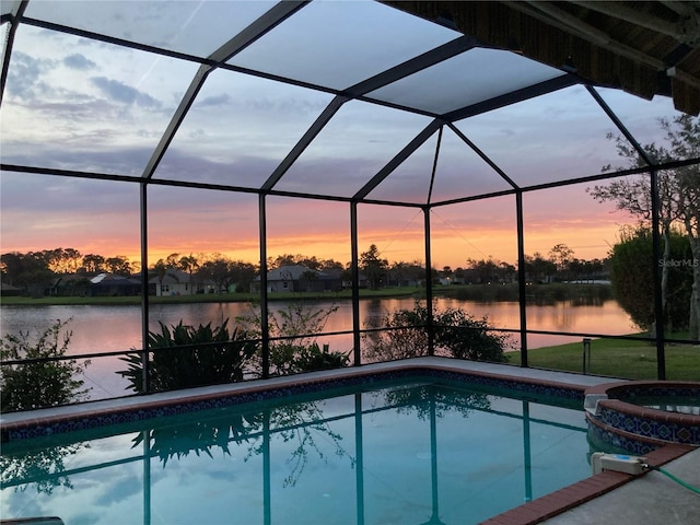 pool at dusk with glass enclosure, an in ground hot tub, and a water view