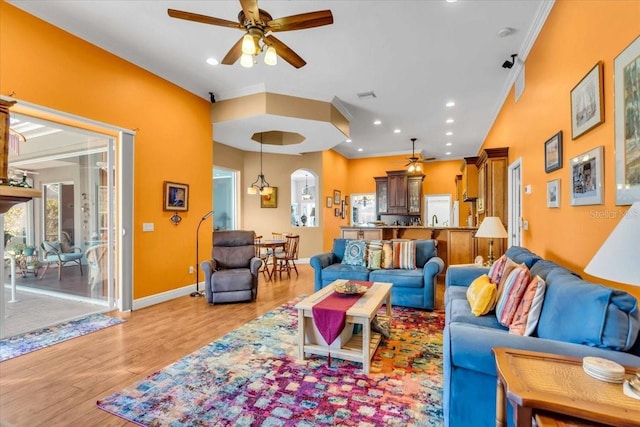 living room featuring ceiling fan with notable chandelier, light wood-type flooring, and crown molding