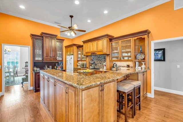 kitchen featuring light stone countertops, light wood-type flooring, backsplash, ornamental molding, and ceiling fan