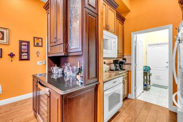 kitchen featuring light wood-type flooring, white appliances, beverage cooler, and dark stone counters