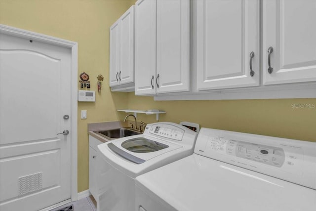 clothes washing area with washing machine and clothes dryer, cabinets, and sink