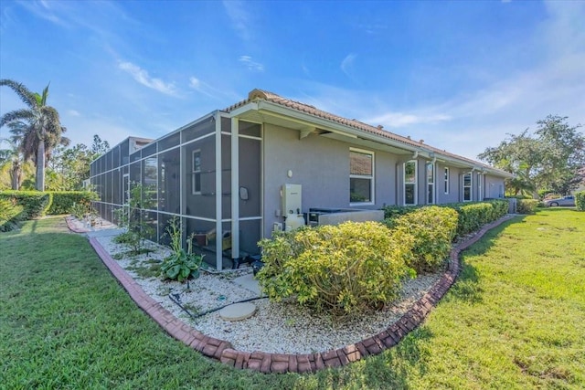 view of side of property featuring a lawn and glass enclosure