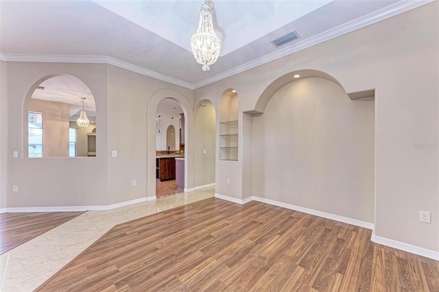 empty room with hardwood / wood-style floors, ornamental molding, and a notable chandelier