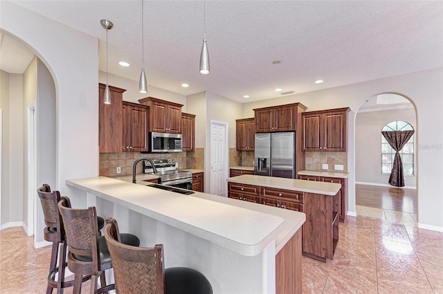 kitchen with a textured ceiling, appliances with stainless steel finishes, decorative light fixtures, kitchen peninsula, and a breakfast bar area