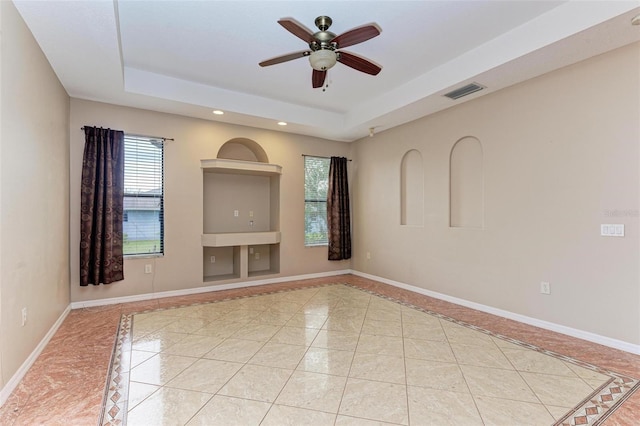 tiled spare room featuring ceiling fan and a tray ceiling