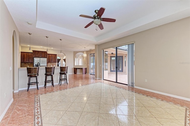 interior space with stainless steel refrigerator with ice dispenser, a kitchen breakfast bar, a raised ceiling, ceiling fan, and pendant lighting