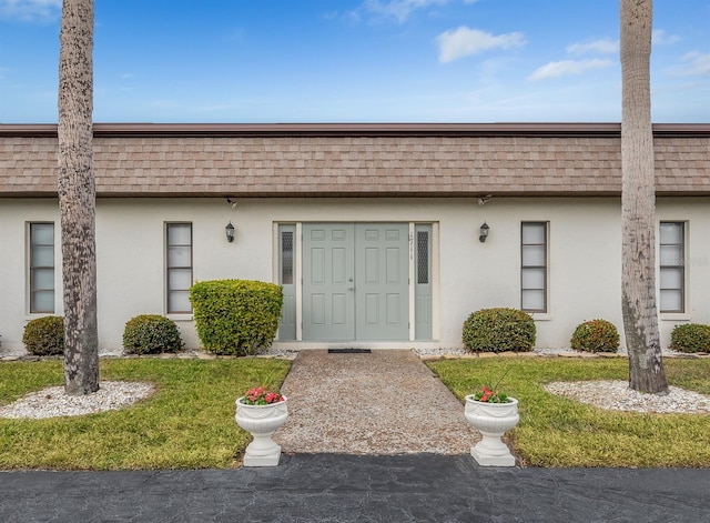 1708 Bonitas Cir Unit 1726A, Venice, FL 34293 - view of exterior entry with mansard roof, stucco siding, a shingled roof, and a yard