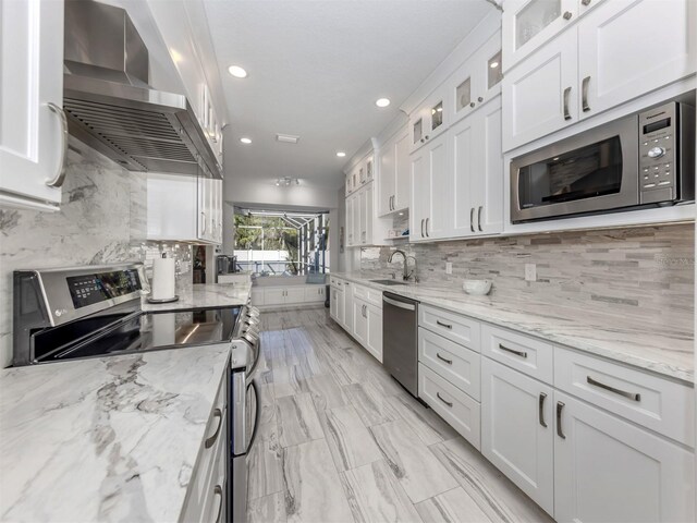 kitchen with white cabinets, appliances with stainless steel finishes, and wall chimney range hood