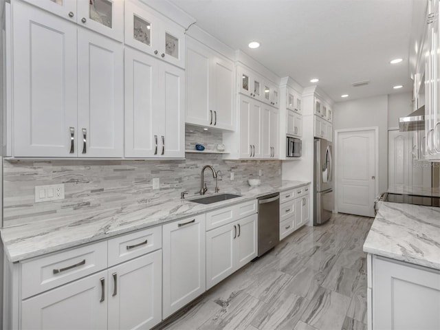 kitchen featuring light stone countertops, white cabinetry, sink, stainless steel appliances, and decorative backsplash