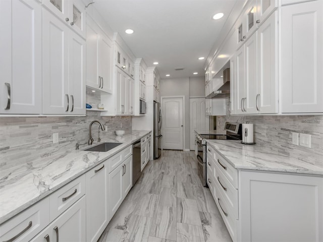 kitchen featuring appliances with stainless steel finishes, white cabinetry, wall chimney exhaust hood, and sink