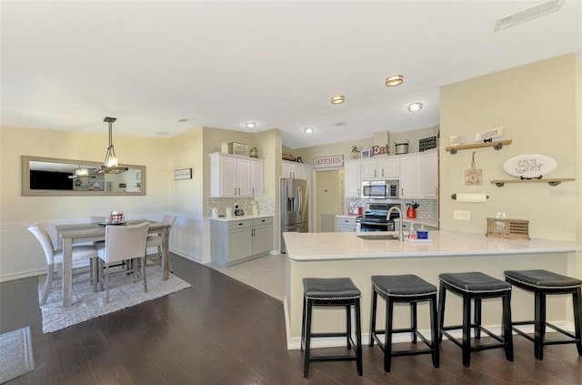 kitchen with kitchen peninsula, tasteful backsplash, stainless steel appliances, dark hardwood / wood-style floors, and white cabinetry