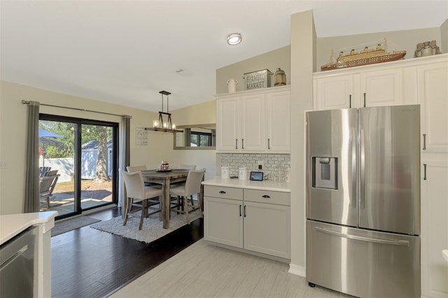 kitchen with white cabinets, stainless steel refrigerator with ice dispenser, light hardwood / wood-style floors, and pendant lighting