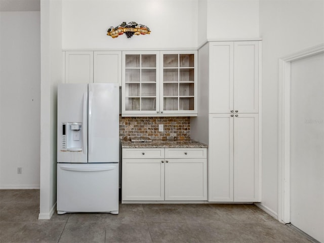 kitchen featuring white refrigerator with ice dispenser, backsplash, dark stone counters, white cabinets, and tile patterned flooring