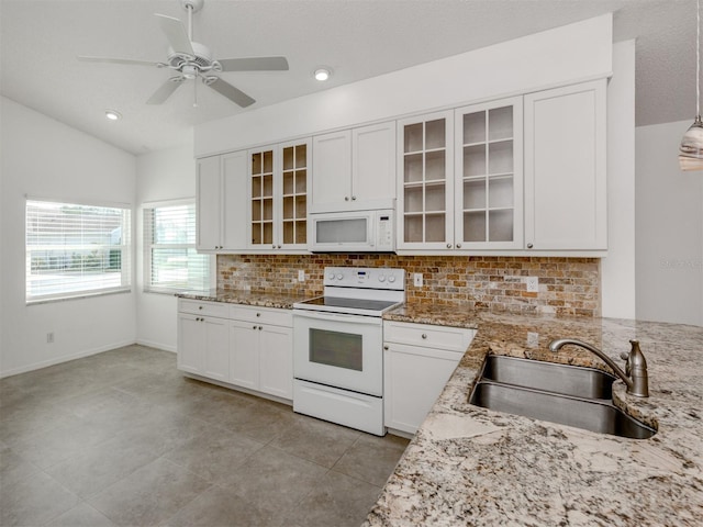 kitchen with sink, light stone counters, vaulted ceiling, white appliances, and white cabinets