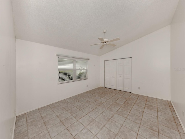 unfurnished bedroom with lofted ceiling, ceiling fan, light tile patterned floors, a textured ceiling, and a closet