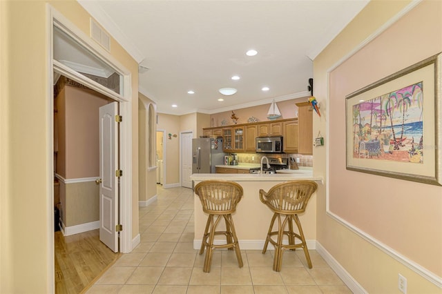 kitchen featuring crown molding, appliances with stainless steel finishes, light tile patterned flooring, a kitchen bar, and kitchen peninsula