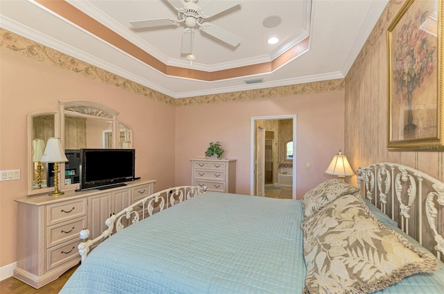 bedroom featuring a raised ceiling, ensuite bath, ceiling fan, ornamental molding, and wood-type flooring