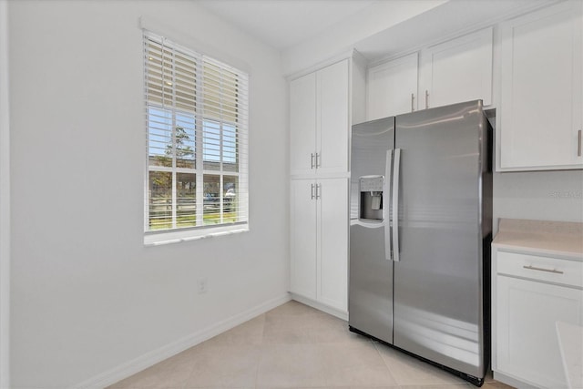 kitchen with stainless steel fridge, light tile patterned floors, and white cabinetry