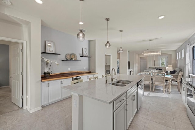 kitchen featuring light stone countertops, stainless steel appliances, sink, white cabinetry, and hanging light fixtures