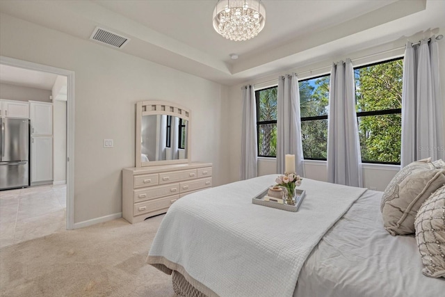 bedroom with a raised ceiling, stainless steel refrigerator, light colored carpet, and an inviting chandelier