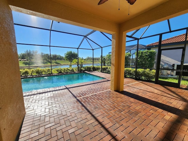 outdoor pool with glass enclosure, a water view, ceiling fan, and a patio area