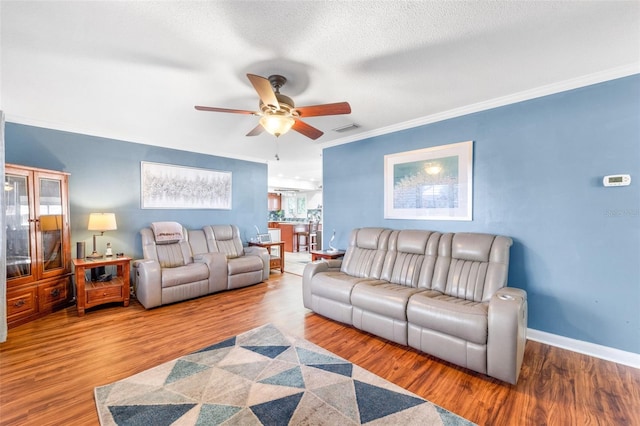 living room featuring ceiling fan, wood-type flooring, a textured ceiling, and ornamental molding