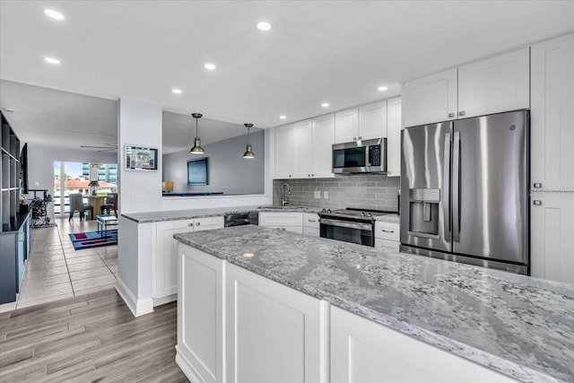 kitchen with kitchen peninsula, light wood-type flooring, stainless steel appliances, pendant lighting, and white cabinets