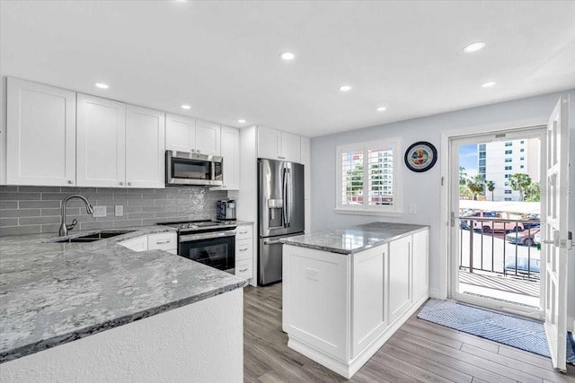 kitchen with white cabinets, kitchen peninsula, stainless steel appliances, and light hardwood / wood-style flooring