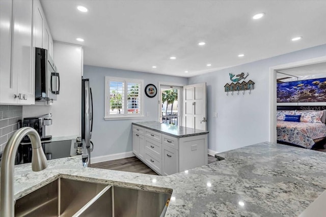 kitchen with white cabinets, sink, light stone counters, kitchen peninsula, and stainless steel appliances