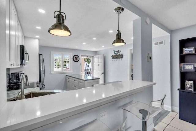 kitchen featuring pendant lighting, sink, kitchen peninsula, appliances with stainless steel finishes, and white cabinetry