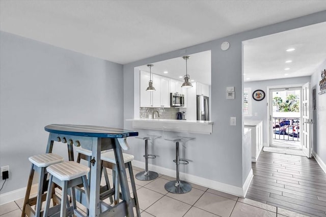 kitchen with hanging light fixtures, stainless steel appliances, kitchen peninsula, white cabinets, and light wood-type flooring