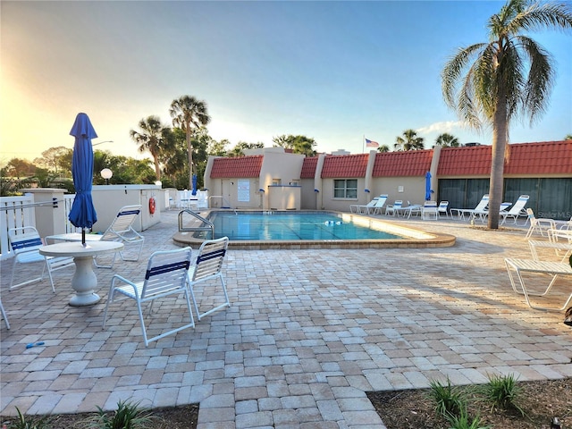 pool at dusk with a community pool, fence, and a patio area
