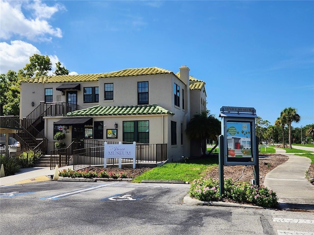 view of front of property featuring uncovered parking, a chimney, stucco siding, and a tiled roof