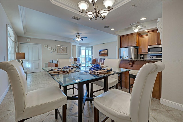 tiled dining space with ceiling fan with notable chandelier, a raised ceiling, and ornamental molding