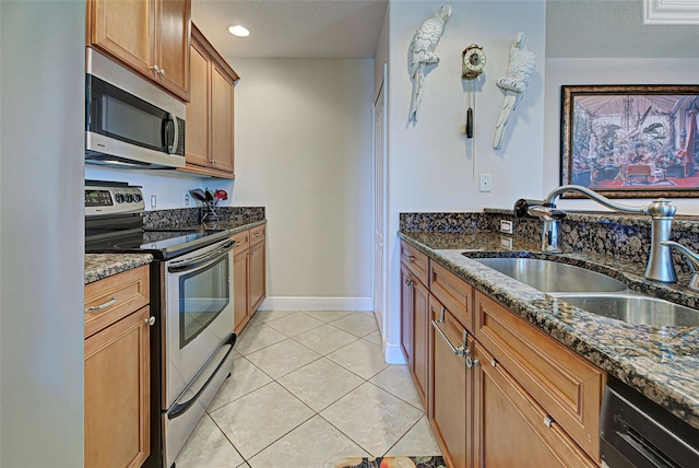 kitchen featuring dark stone countertops, light tile patterned floors, sink, and appliances with stainless steel finishes