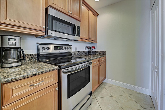 kitchen featuring light tile patterned floors, stainless steel appliances, and dark stone counters