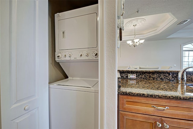 laundry room with crown molding, stacked washer and dryer, and a chandelier