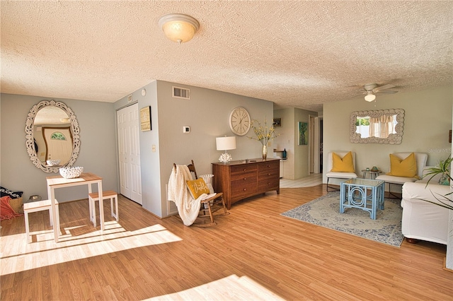 living room with ceiling fan, wood-type flooring, and a textured ceiling