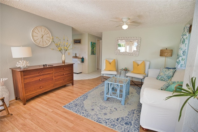 living room with ceiling fan, a textured ceiling, and light hardwood / wood-style flooring