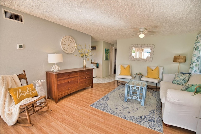 living room featuring ceiling fan, light hardwood / wood-style floors, and a textured ceiling